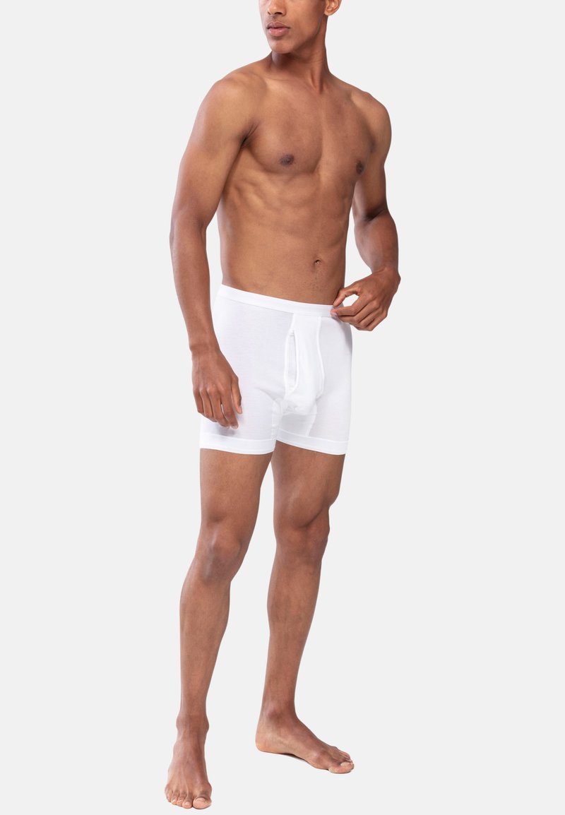 Hvide bomulds boxershorts med en tætsiddende design, der har en elastisk talje og en funktionel gylp, vist på en model med en neutral baggrund.