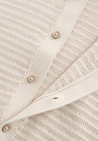 Beige strikket cardigan med tekstureret design, knaplukning og ribstrikkede kanter. Inklusive store, neutrale knapper.
