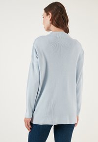 Világoskék, hosszú ujjú pulóver, laza szabással, bordás textúrával és kerek nyakkivágással, sötét farmernadrággal párosítva.