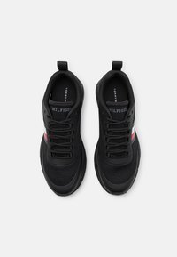 Chaussures de sport noires avec une tige en mesh, un système de laçage à six œillets, et un accent rayé rouge et blanc sur le côté.