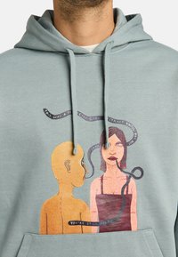Lichtgroene hoodie met een voorkantgrafiek van een naakt figuur en een vrouw, beide geïllustreerd met tekst en fijne details. Zachte textuur, capuchon met trekkoord.