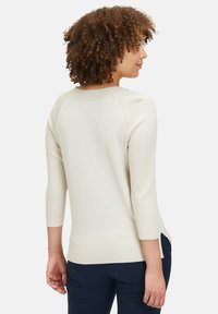 Helle beige Strickjacke mit geripptem Design, Dreiviertelärmeln und seitlichen Schlitzen. Zarte Textur mit einem lässigen Ausschnitt und tailliertem Saum.