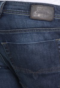 Mörkblå jeans i denim med en läderlapp märkt "DIESEL." Har en klassisk fickdesign och kontrasterande sömmar.