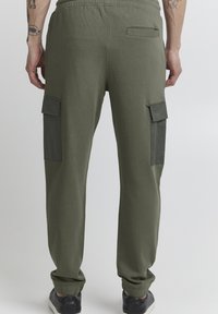 Green cotton joggers with a relaxed fit, featuring cargo pockets on the sides and a rear patch pocket. Soft texture, elastic waistband.