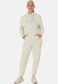 Beige hoodie with a front pocket and drawstring hood, paired with matching tapered sweatpants. Both made of soft, textured fabric.