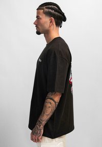 Zwarte katoenen t-shirt met een relaxte pasvorm, met een grafisch ontwerp op de achterkant. Soepele textuur, korte mouwen en een ronde hals.