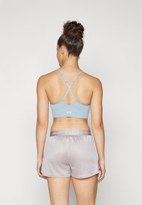 Lichtblauwe sportbh met gekruiste bandjes, gecombineerd met grijze mesh shorts met een merkband.