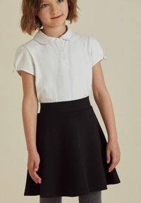 Schwarzer A-Linien-Rock mit glatter Textur und elastischem Bund, kombiniert mit einem weißen Polo-Shirt mit Kragen und Knopfleiste.