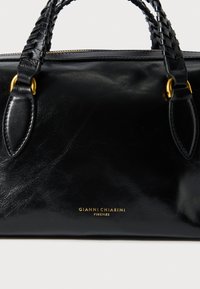 Mustast nahast käekott punutud sangadega, kuldse riistvaraga ja reljeefse logoga. Sile tekstuur täiustab klassikalist ja elegantset välimust.