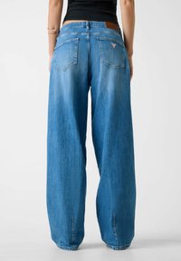Jeansy o szerokich nogawkach w jasnoniebieskim dżinsie z wyblakłą fakturą. Posiadają skórzaną naszywkę, dwie tylne kieszenie oraz trójkątne logo na plecach.