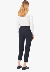 Pantalons tailleur bleu marine avec une coupe slim, longueur cheville, deux poches à l'arrière et une texture lisse, associés à un chemisier blanc et des ballerines noires.