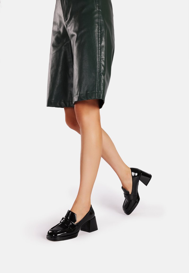 Mocassini con tacco in pelle verniciata nera, a punta quadrata, con una piccola fascia decorativa e un tacco spesso e quadrato.