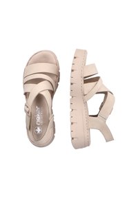 Sandales plateforme beiges avec un design à strap croisé, en cuir lisse. Elles possèdent une semelle texturée et une fermeture à boucle sur le côté.