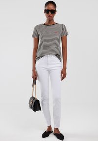 Camiseta de manga corta a rayas en blanco y negro combinada con jeans ajustados blancos. Gafas de sol negras y un bolso negro con detalles dorados.