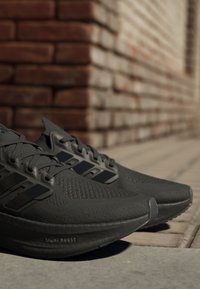 Crne sportske cipele s teksturiranim materijalom, plastičnim detaljima i prepoznatljivom "Light Boost" značajkom na potplatu. Elegantna, moderna dizajn.