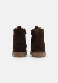 Hnědé semišové kotníkové boty s polstrovaným límcem, dvěma poutky na nazouvání a gumovou podrážkou s texturovaným vzorem běhounu.