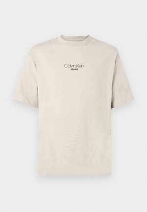 Bež majica kratkih rukava s okruglim izrezom s logotipom "Calvin Klein JEANS" centriranim na prsima.