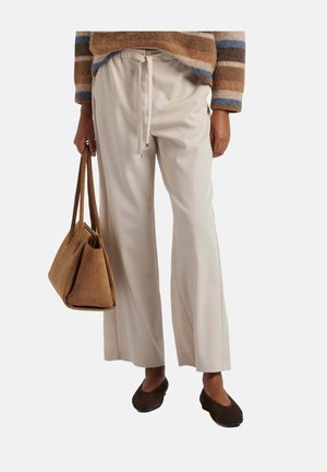Persoon draagt crèmekleurige brede broekspijpen en bruine platte schoenen, houdt een bruine suède handtas vast, met een gedeeltelijk zichtbare gestreepte trui.