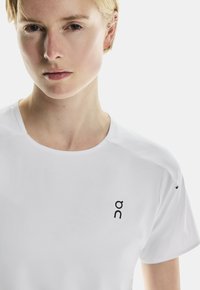 T-shirt de sport blanc pour homme avec des manches courtes, présentant un logo noir sur le côté gauche, en tissu lisse et avec un col rond.