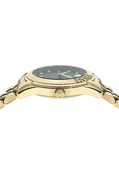 Arany színű karóra textúrázott fekete számlappal, gyémánt órajelzőkkel, bordázott lünetta és láncos karkötő jellemzi. Arany koronával rendelkezik.