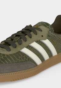 Πράσινο υφασμάτινο παπούτσι Adidas Samba με λευκές ρίγες, λαστιχένια σόλα και σκούρα πράσινα κορδόνια, εμφανίζεται σε κοντινή γωνιακή όψη.