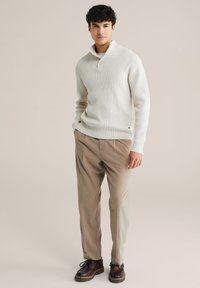 Svijetlosivi džemper od wafl pletenja s ovratnikom i detaljem s gumbima, u kombinaciji s bež hlačama i smeškim cipelama na vezanje. Glatka tekstura, ležeran kroj.