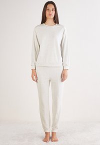Lichtgrijze sweatshirt en bijpassende broek gemaakt van zachte stof. De top heeft een ronde halslijn, terwijl de broek aansluitende boorden bij de enkels heeft.