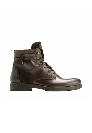 Bottine en cuir marron avec semelle noire, col en tissu, œillets métalliques et fermeture à lacets, présentée de profil sur fond blanc.