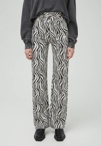 Pantalon large à motif zèbre en noir et blanc, avec taille haute, texture semblable au denim et poches apparentes. Associé à des bottes noires.