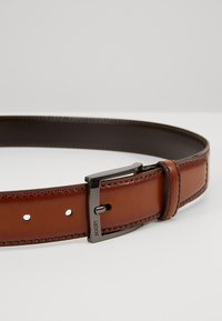 Cintura in pelle marrone con una finitura liscia, fibbia in metallo color argento e cuciture visibili. Regolabile con più fori per una vestibilità.