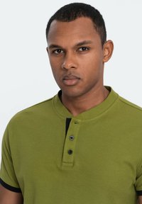 Polo di colore verde oliva con patta dei bottoni e colletto neri, dotato di maniche corte e tessuto texturizzato.