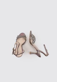 Sandales à talons marron avec un design ouvert à l'avant, ornées d'accents métalliques et de brides de cheville ajustables. Détails de surface texturée.
