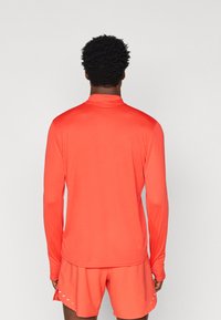 Long-sleeve shirt in bright coral, made of smooth, stretch fabric. Features a stand-up collar and fitted design, paired with matching shorts.