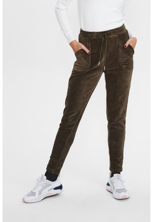 Pantalon de jogging en velours côtelé marron avec poches avant et cordon de serrage, porté avec des baskets blanches et un haut à manches longues blanc.