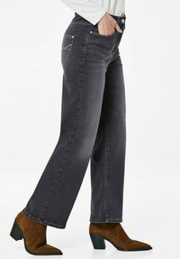 Jean gris foncé avec une coupe droite, présentant une taille mi-haute et des poches arrière. Porté avec des bottines à talons marron.