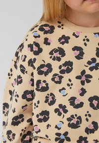 Felpa beige con un motivo floreale nero e accenti rosa e blu. Tessuto morbido con una vestibilità rilassata e colletto a costine.