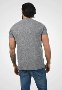 Grå kortermet t-skjorte laget av teksturert stoff, tettsittende stil, med rund hals. Kombinert med blå jeans med dekorativ søm på lommene.