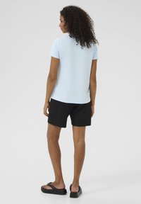 Lichtblauw t-shirt met korte mouwen gecombineerd met zwarte shorts. Het t-shirt heeft een ronde halslijn, terwijl de shorts een eenvoudig ontwerp hebben. Zwarte slippers maken de outfit compleet.