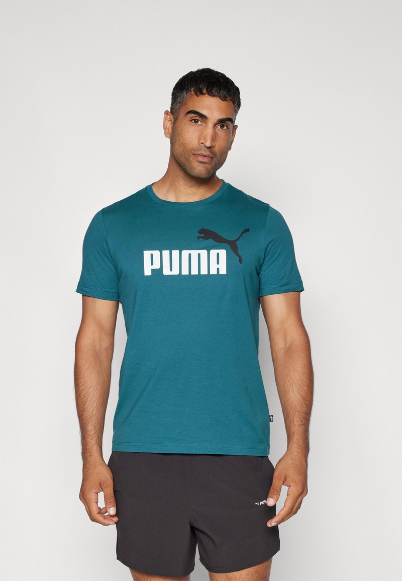 Mėlynos spalvos medvilninis marškinėliai turi didelį baltą "PUMA" logotipą ir juodą Pumos katės dizainą kairėje krūtinės pusėje. Trumpi rankoviai ir apvalus iškirpimas.