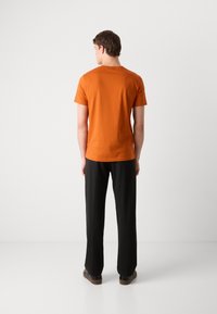 Kortermet, rundhalset t-skjorte i livlig oransje bomull, kombinert med svarte, rettlånede bukser og svarte sneakers.