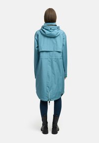 A long, light blue raincoat with a hood, featuring a loose fit, cinched waist, and pockets, paired with dark jeans and black boots.