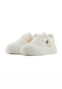 Zapatillas de piel blanca con suela gruesa y texturizada, que presentan acentos dorados y un diseño cosido. Atadas con seis ojales y detalles perforados.