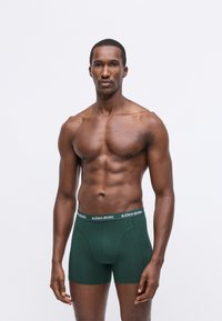 Boxer in cotone verde con vita elastica e logo "BJÖRN BORG". Texture liscia e design aderente. Il modello è in piedi di fronte.