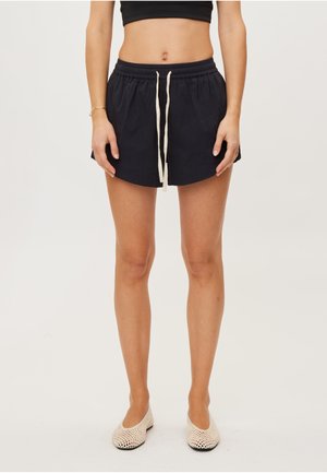 Ciemnogranatowe szorty z elastycznym pasem i sznurkiem, o luźnym kroju i gładkiej fakturze. Połączone z jasnymi, płaskimi butami.