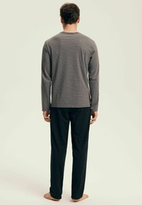 Langärmliges graues Hemd mit weißen Streifen, kombiniert mit schwarzen Hosen. Der Stoff wirkt weich, hat einen lässigen Schnitt und keine sichtbaren Muster.