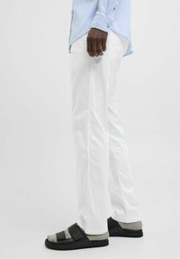 Bílé lněné kalhoty, světle modrá košile na knoflíky, černé sandály s šedými detaily a texturovanou podrážkou. Důraz na čisté linie a pohodlný střih.