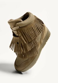 Bruine high-top schoenen met een mix van suède en stof, versierd met lange franjes bij de enkel, en een gestructureerde rubberen zool.