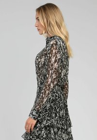 Robe noire et blanche à motifs, transparente, avec des manches longues, un ourlet froncé, un col haut et une taille cintrée. Présente des textures et des couches variées.