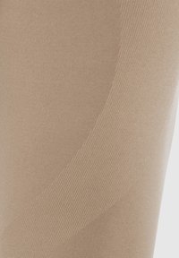Collant beige con una texture liscia, caratterizzati da un sottile design a costine e un motivo curvo per un interesse visivo aggiuntivo.