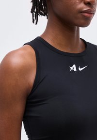 Κοντινό πλάνο ενός ατόμου που φοράει μαύρο αμάνικο αθλητικό τοπ με λευκά λογότυπα Nike και άλλα στο στήθος.